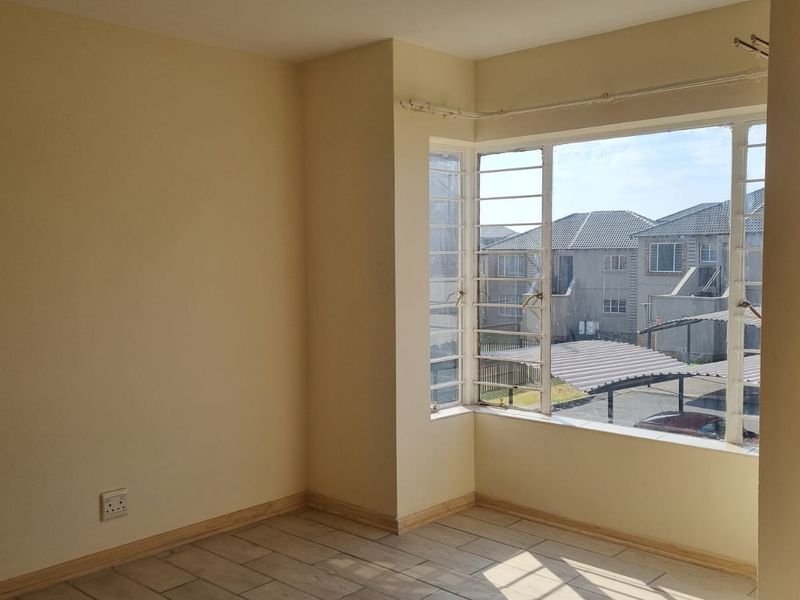 An empty bedroom featuring tiled flooring, neutral walls, and large metal-framed windows providing natural light and a view of the complex.