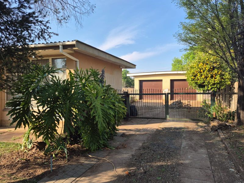 Front exterior view of the property featuring a paved driveway, metal security gate, and a detached double garage with roller doors.