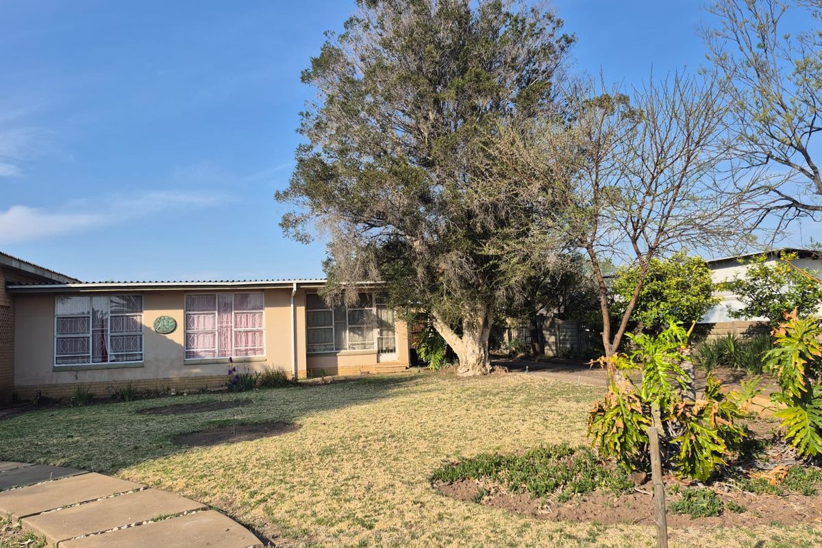 A view of the rear exterior of the house featuring a large mature tree, a paved walkway, and a spacious garden area.