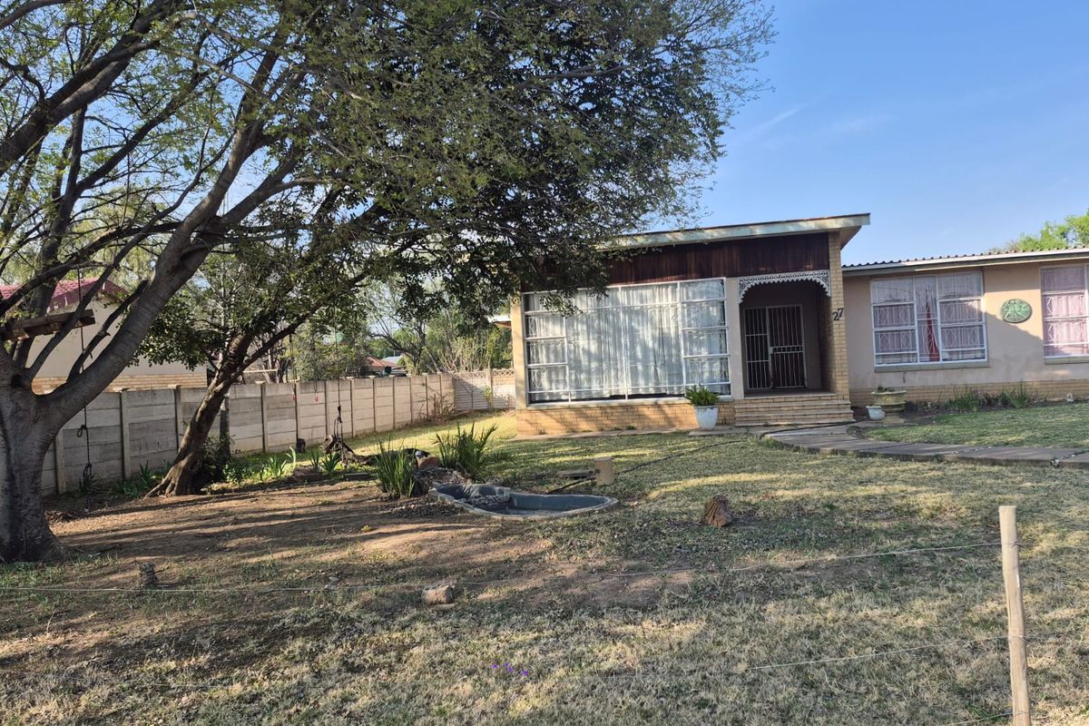 Front view of a single-story house featuring a brick facade, security gate, paved walkway, and a spacious front garden with a small pond.
