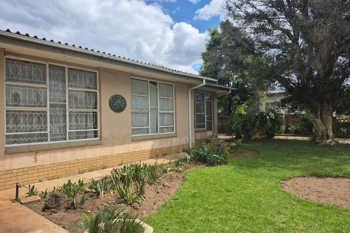 Rear exterior view of the house featuring a lawn, garden beds, and plastered walls with metal security bars on the windows.