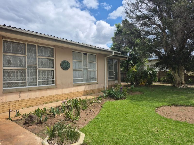 Rear exterior view of the house featuring a lawn, garden beds, and plastered walls with metal security bars on the windows.
