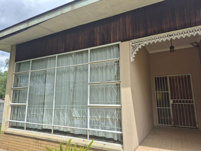Front facade featuring a large steel-framed window with security bars, decorative metal fretwork, and a covered porch area with tiled flooring.