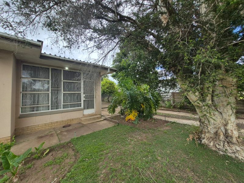 Rear exterior view of the property featuring a paved area, security gates, and established garden with mature trees.