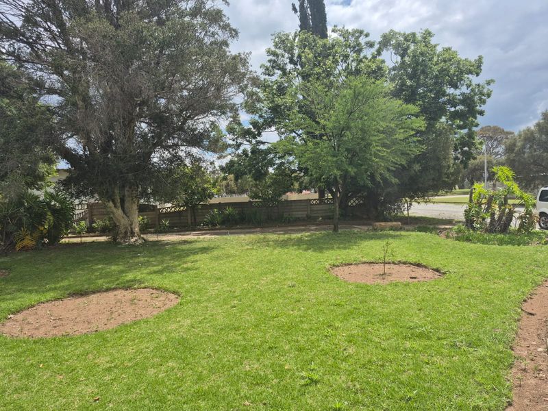 A spacious, well-maintained garden featuring a lush green lawn, mature trees, and a secure precast concrete boundary wall.