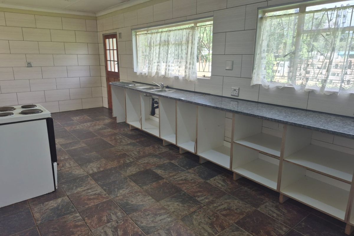 Spacious kitchen featuring tiled walls and flooring, granite countertops, and a stainless steel sink, currently awaiting cabinetry doors and finishing touches.