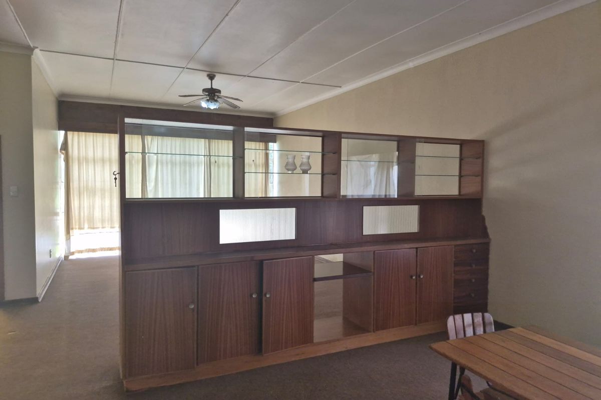 Spacious living area featuring a large built-in wooden room divider, ceiling fan, and neutral wall finishes, offering potential for modern updates.