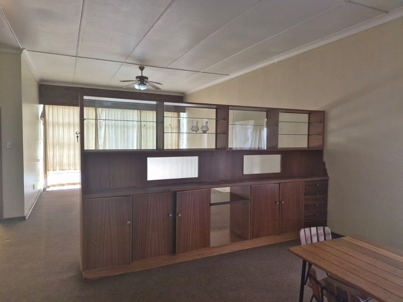 Spacious living area featuring a large built-in wooden room divider, ceiling fan, and neutral wall finishes, offering potential for modern updates.