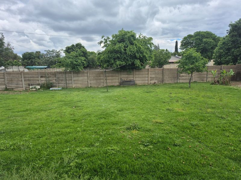 A spacious, level backyard featuring a well-maintained lawn enclosed by a precast concrete boundary wall.