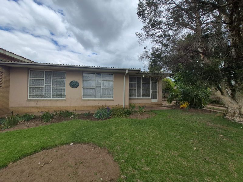Rear view of the house featuring a brick facade, large windows with security gates, and a spacious garden area with a mature tree.