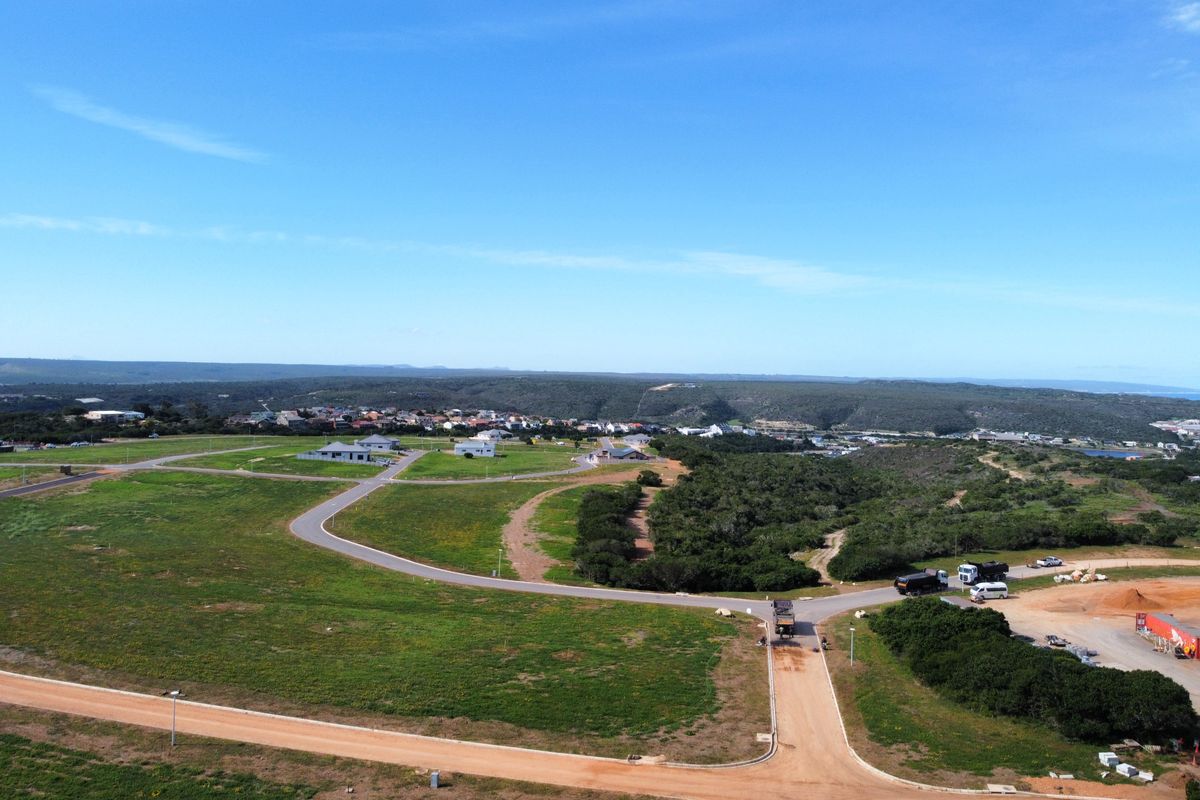 An aerial view of a residential development site featuring paved and dirt roads, surrounding natural vegetation, and distant housing.