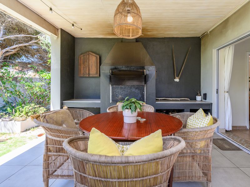 Covered outdoor patio featuring a built-in braai, tiled flooring, and timber ceiling, providing a seamless transition to the garden area.
