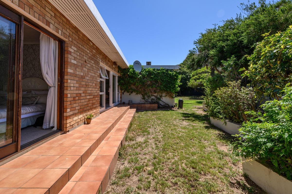 Rear exterior view featuring a brick facade, tiled patio area, and a garden with established landscaping and raised beds.