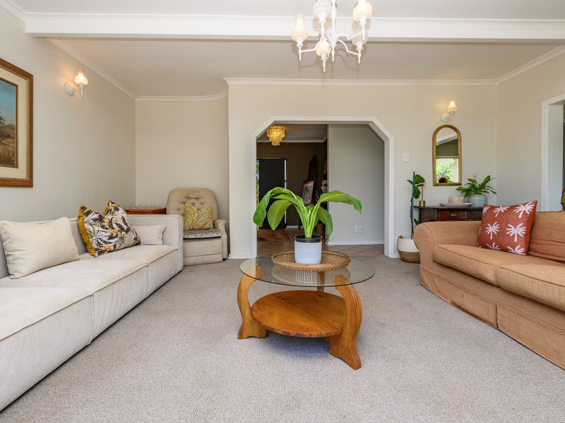 A spacious living room featuring neutral wall tones, a decorative ceiling beam, and a classic archway leading to the entrance hall.
