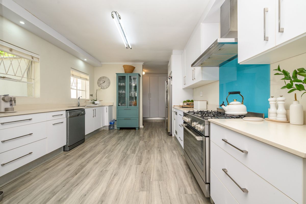 Modern galley-style kitchen featuring white cabinetry, gas stove with extractor fan, blue glass splashback, and light wood-look laminate flooring.