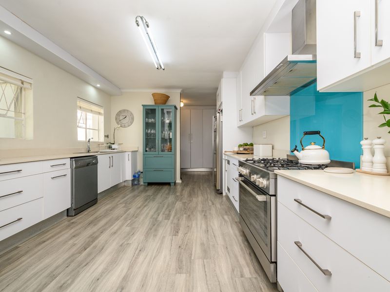 Modern galley-style kitchen featuring white cabinetry, gas stove with extractor fan, blue glass splashback, and light wood-look laminate flooring.