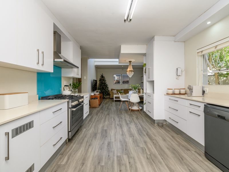 Modern open-plan kitchen featuring white cabinetry, gas stove, and laminate flooring, seamlessly flowing into the adjacent dining and living area.