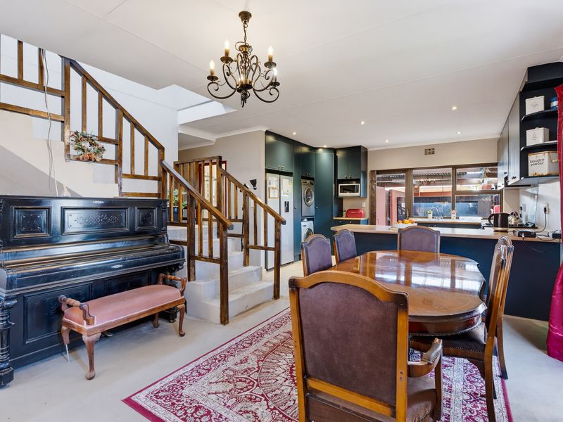An open-plan living and dining area featuring a wooden staircase, modern dark kitchen cabinetry, and direct access to the outdoor patio through sliding doors.