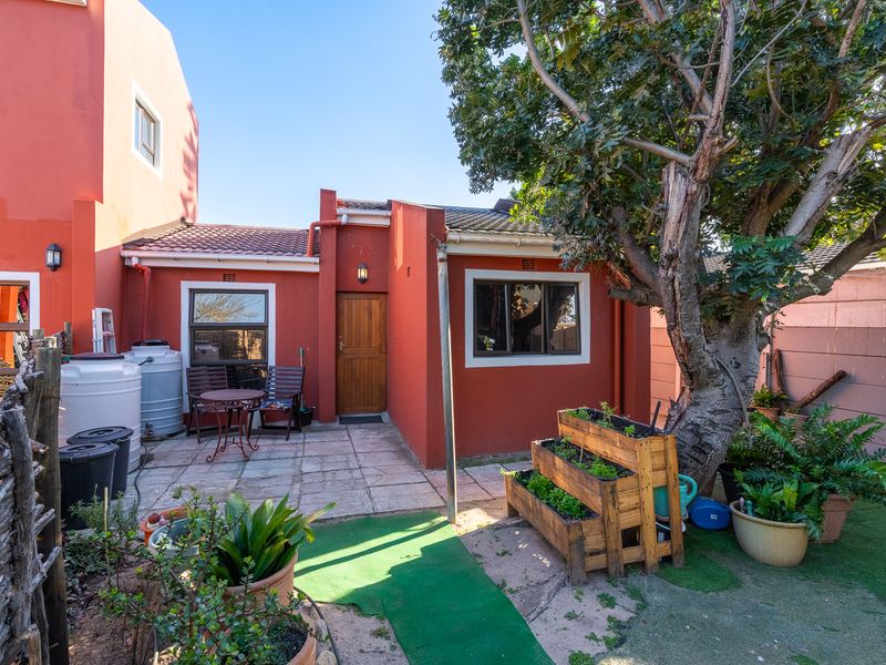 Rear exterior view featuring a paved patio area, mature tree, and access to the home via a timber door.