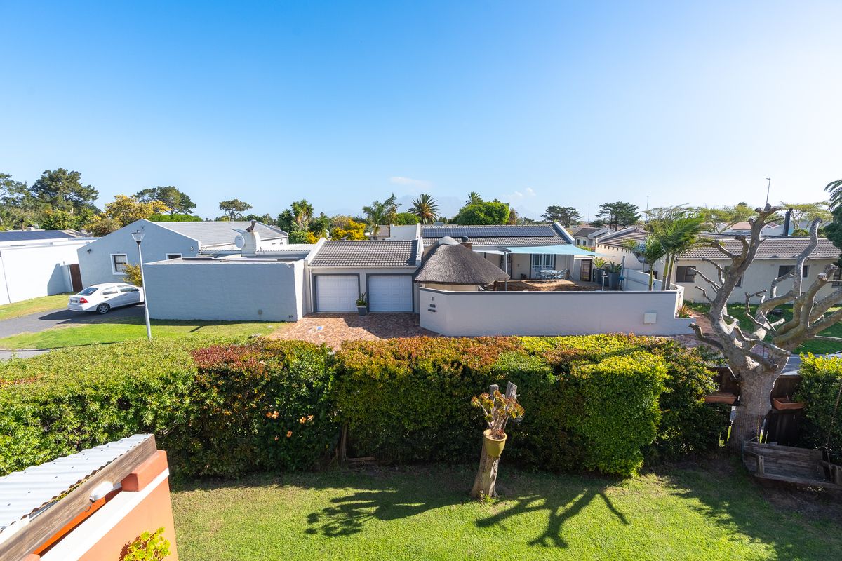Aerial view of a residential property featuring a double garage, solar panels, a thatched roof section, and a paved driveway.