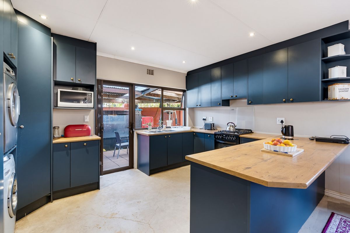 Modern kitchen featuring dark blue cabinetry, wooden countertops, integrated appliances, and a central island, with direct access to the rear patio area.