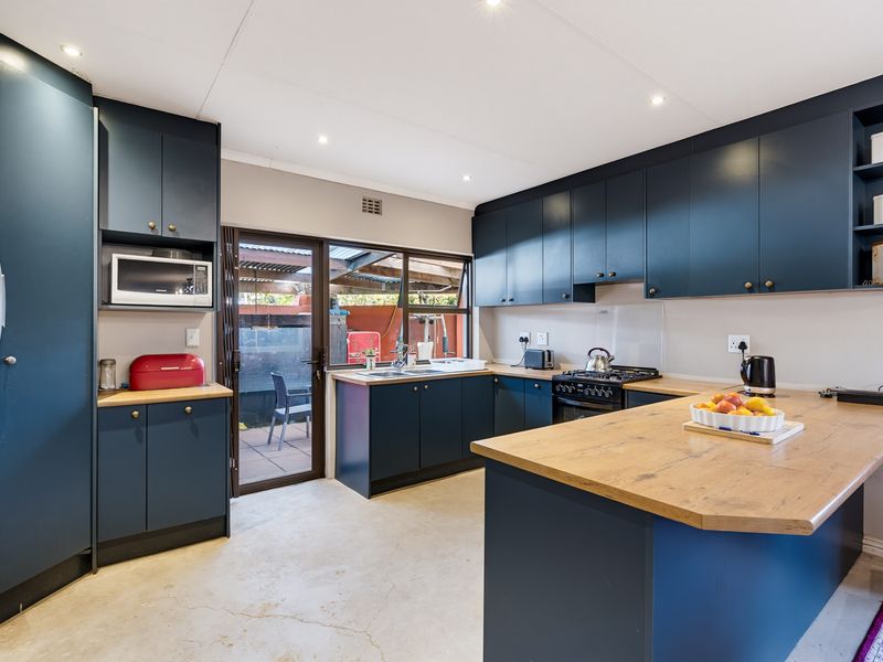 Modern kitchen featuring dark blue cabinetry, wooden countertops, integrated appliances, and a central island, with direct access to the rear patio area.
