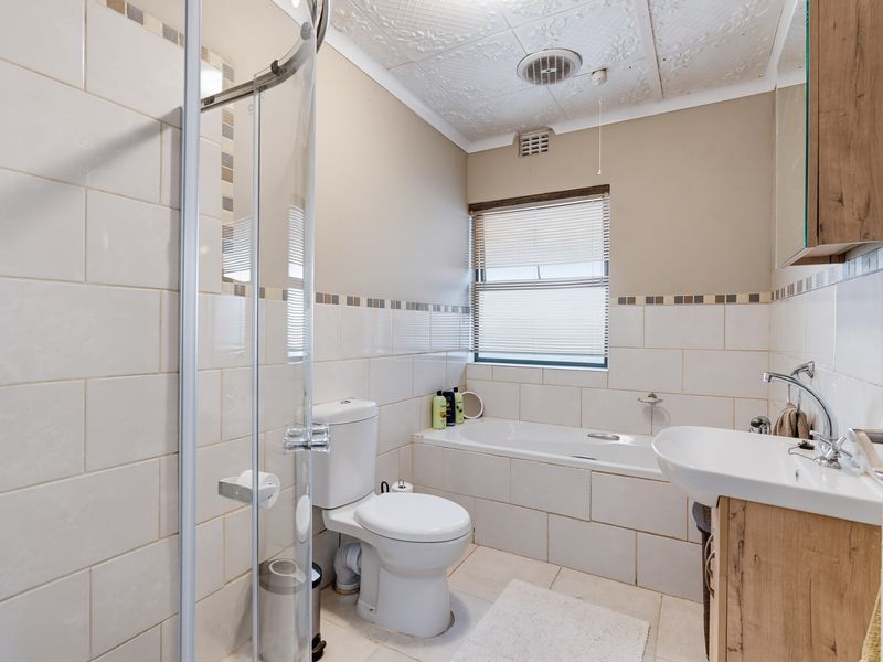 A functional bathroom featuring a shower enclosure, bathtub, toilet, and vanity basin with neutral wall tiling and a textured ceiling.