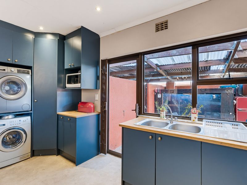 Functional laundry room featuring dark blue built-in cabinetry, a double sink with countertop, and space for stacked laundry appliances.