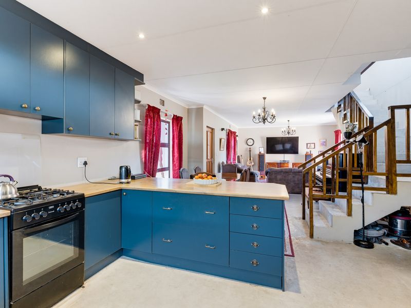 Open-plan kitchen featuring blue cabinetry and a gas stove, flowing into a living area with a wooden staircase.