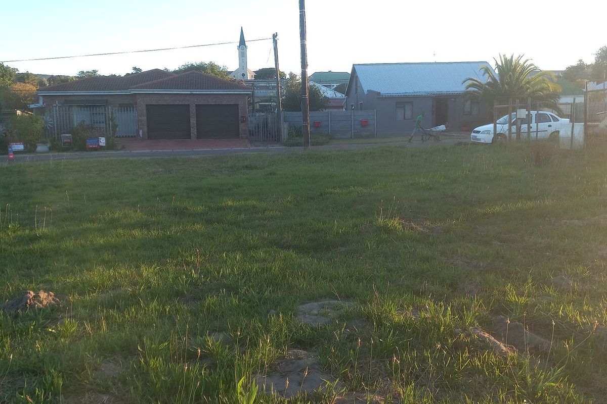 A vacant residential plot of land featuring a grass lawn, situated in a developed neighborhood with surrounding residential properties.