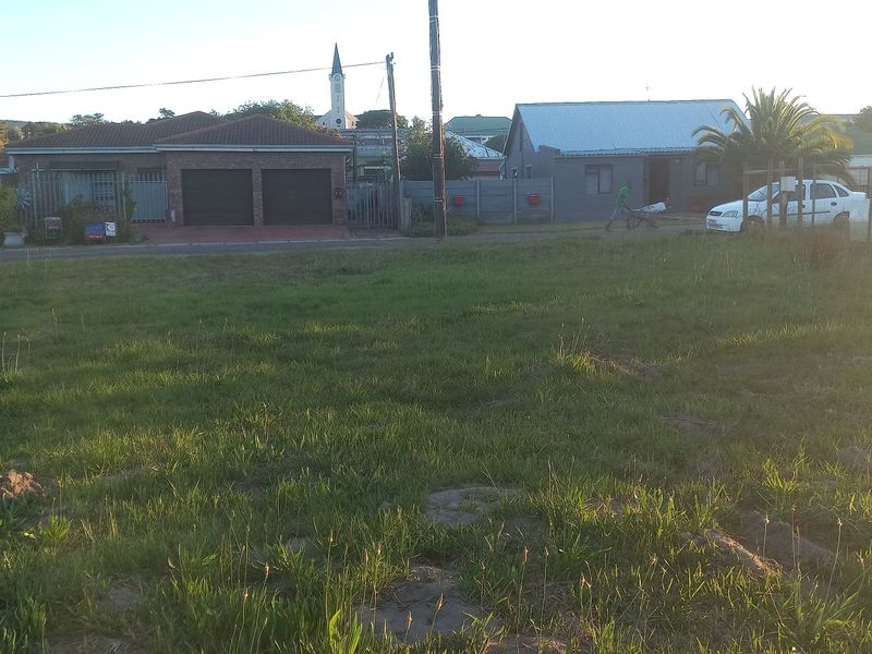 A vacant residential plot of land featuring a grass lawn, situated in a developed neighborhood with surrounding residential properties.