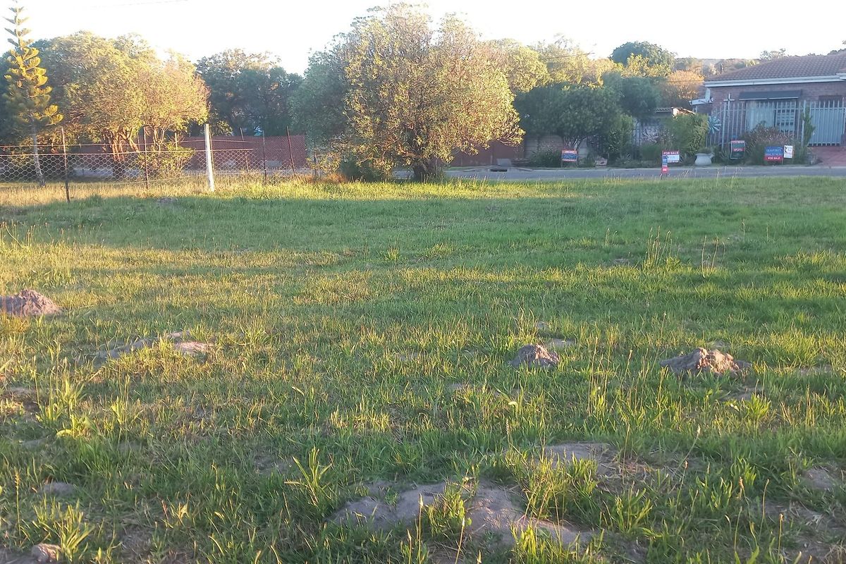 A vacant residential plot featuring a grass lawn and wire mesh perimeter fencing, situated in a developed neighborhood.