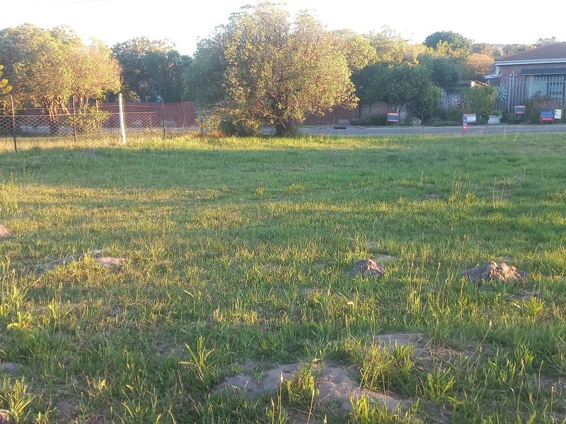 A vacant residential plot featuring a grass lawn and wire mesh perimeter fencing, situated in a developed neighborhood.
