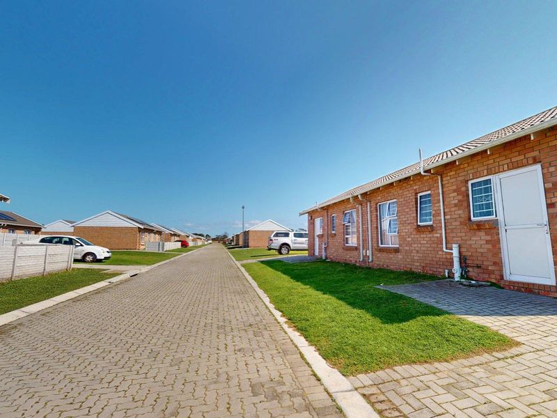 A street view of a residential townhouse complex featuring face brick exteriors, paved driveways, and well-maintained lawns under a clear blue sky.