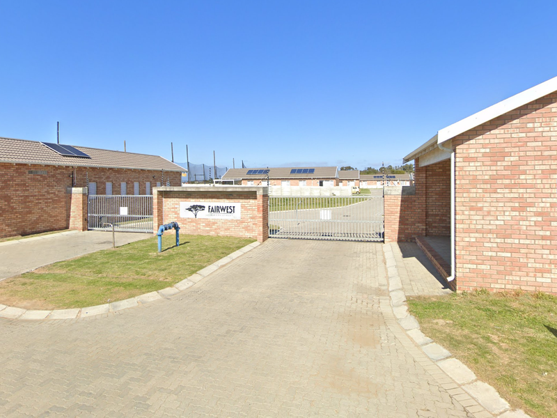 The entrance to the Fairwest estate features a secure gated access point with brick buildings, paved driveway, and perimeter electric fencing.