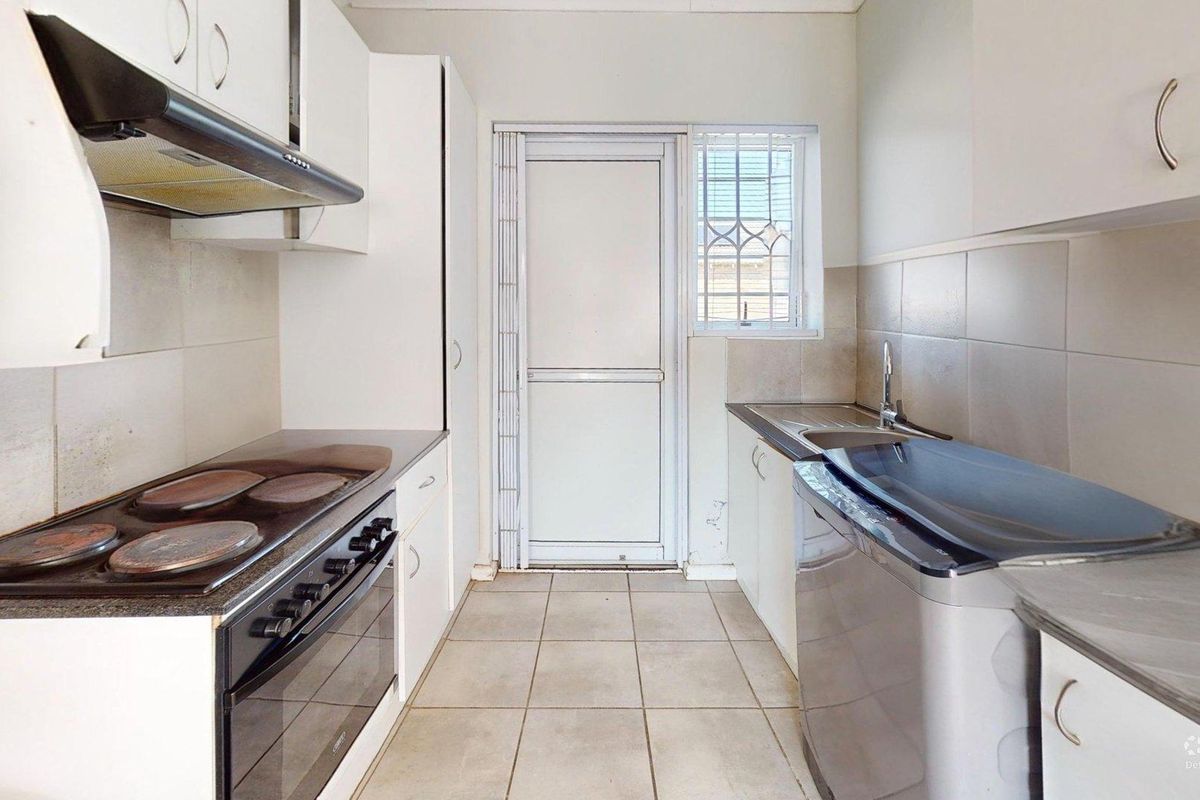 A functional galley-style kitchen featuring built-in cabinetry, an electric stove with extractor fan, tiled backsplash, and direct access to the exterior.