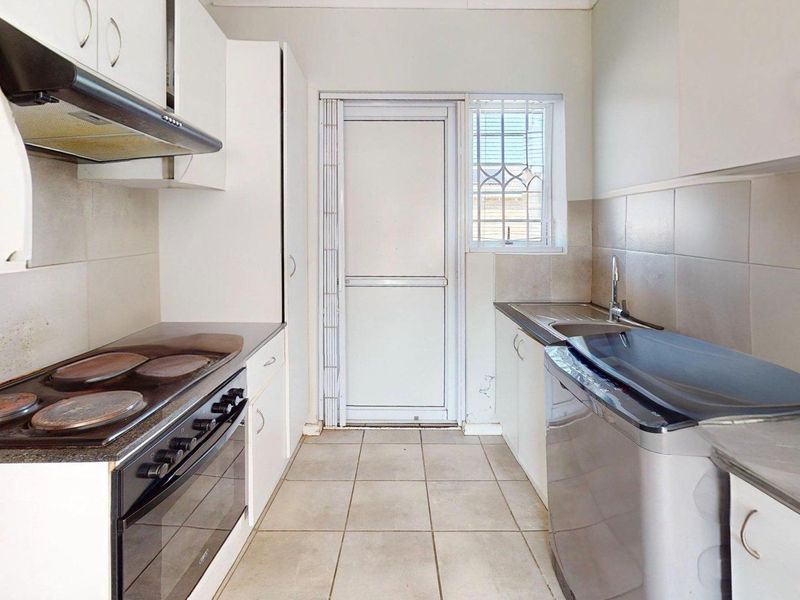 A functional galley-style kitchen featuring built-in cabinetry, an electric stove with extractor fan, tiled backsplash, and direct access to the exterior.