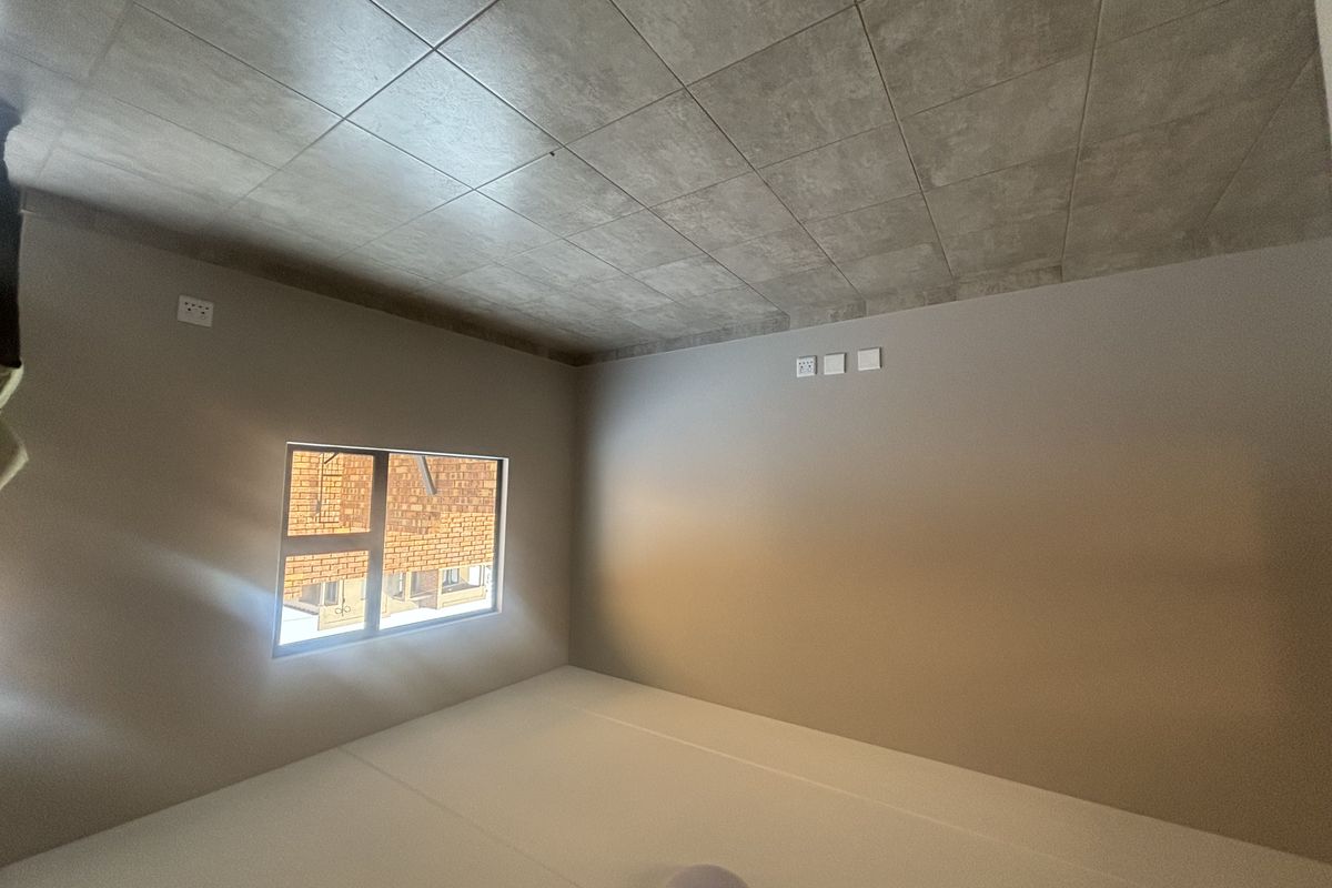 A clean, empty bedroom featuring neutral wall paint, large tiled flooring, and a modern aluminium window frame, providing a blank canvas for personalization.