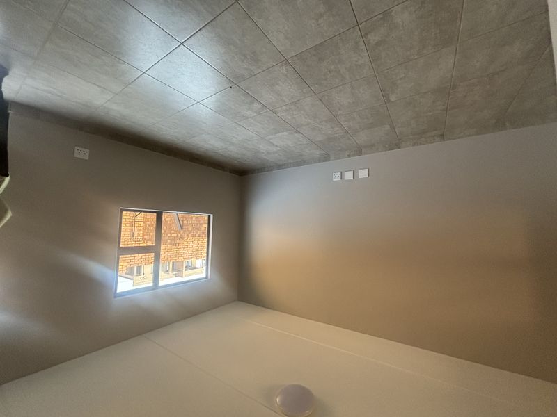 A clean, empty bedroom featuring neutral wall paint, large tiled flooring, and a modern aluminium window frame, providing a blank canvas for personalization.