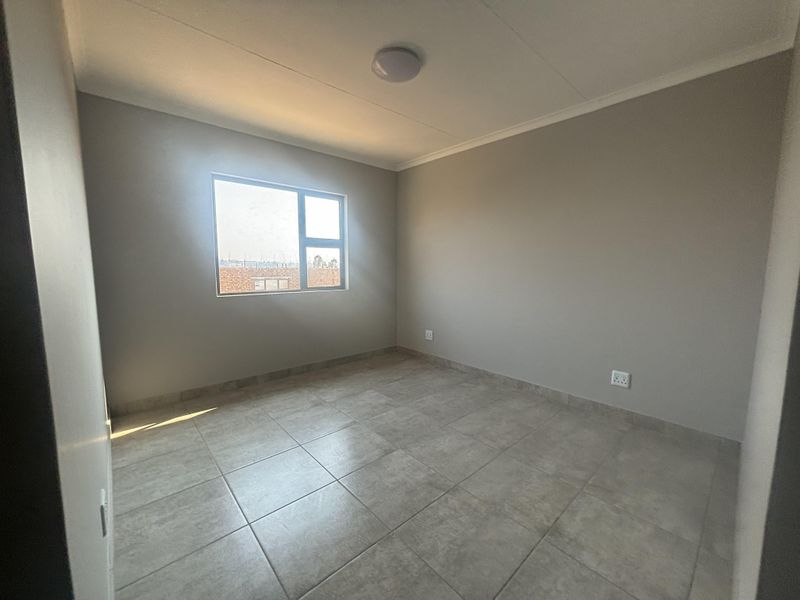 A clean, empty bedroom featuring neutral wall paint, tiled flooring, and a large window providing natural light.