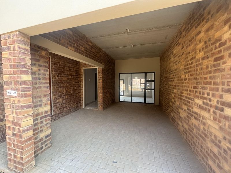 An unfinished garage space featuring exposed brick walls, paved flooring, and a sliding glass door leading to the interior.