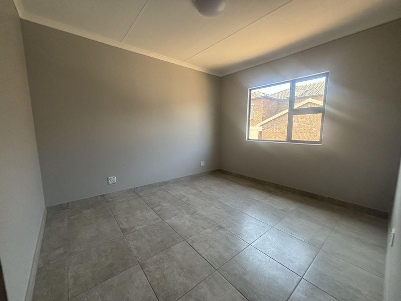 A clean, empty bedroom featuring neutral grey walls, large format floor tiles, and a modern aluminium window frame.
