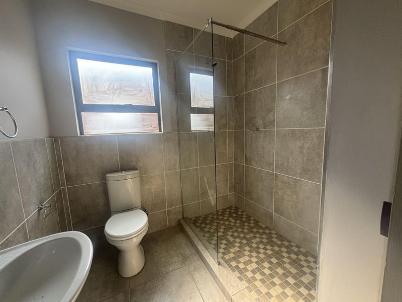A modern bathroom featuring a walk-in shower with a glass screen, tiled walls and flooring, a pedestal basin, and a standard toilet.