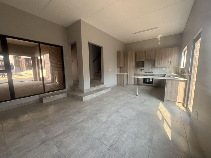Spacious open-plan living and kitchen area featuring modern cabinetry, integrated appliances, tiled flooring, and large sliding doors leading to an outdoor patio.