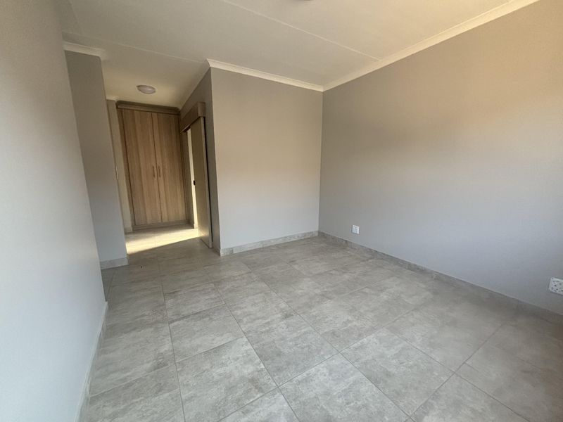 A clean, empty bedroom featuring neutral grey walls, modern tiled flooring, and built-in wooden cupboards.