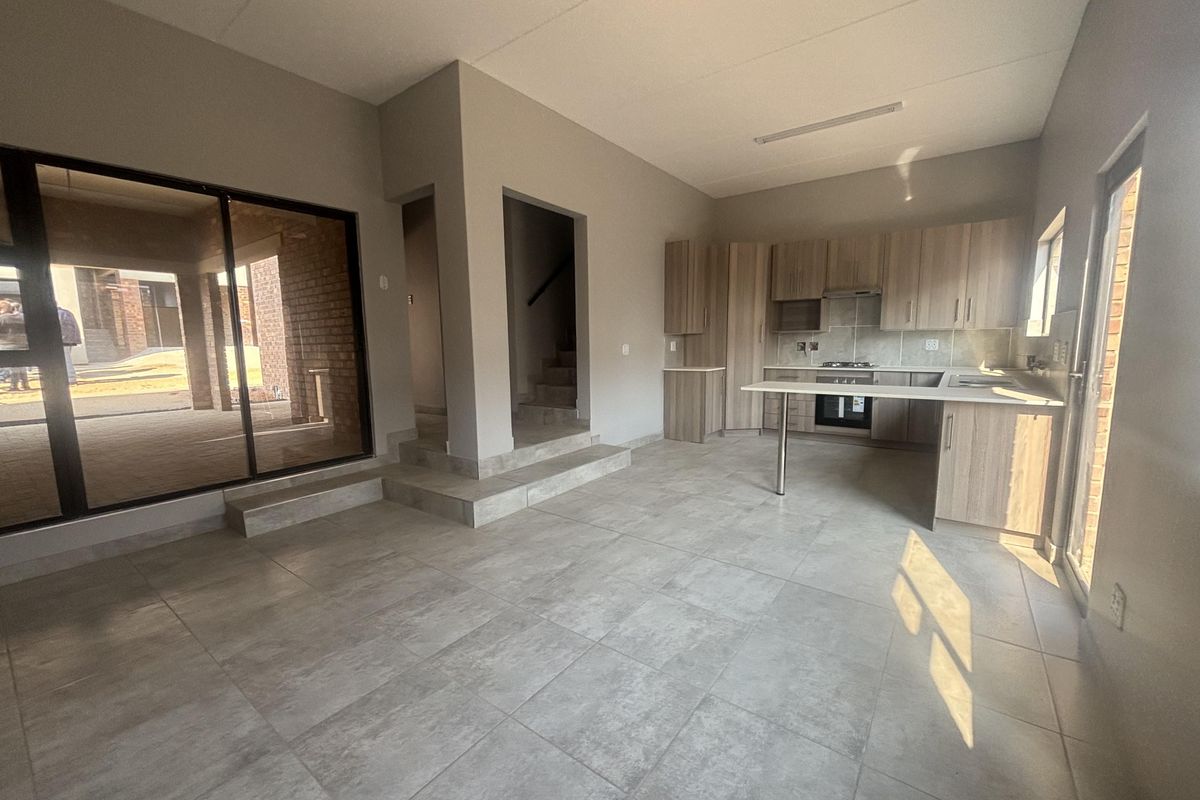 Spacious open-plan living and kitchen area featuring modern cabinetry, integrated appliances, tiled flooring, and large sliding doors leading to an outdoor patio.
