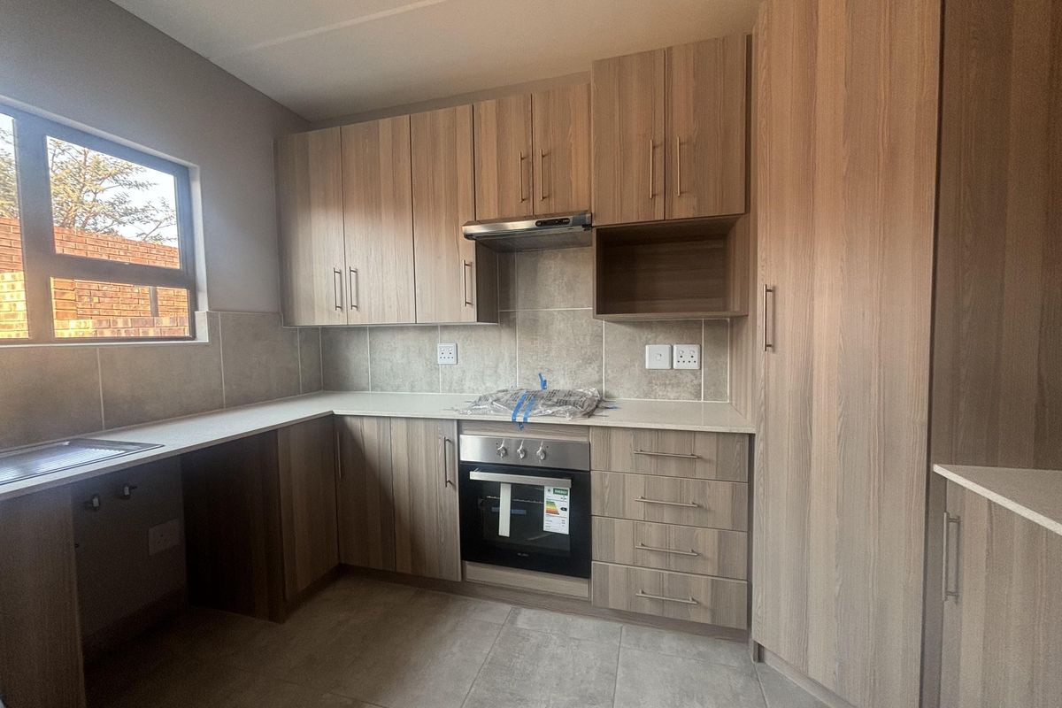 Modern kitchen featuring light wood-grain cabinetry, stone countertops, built-in oven, extractor fan, and neutral tiled flooring in a clean, contemporary finish.