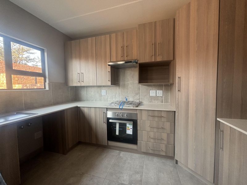 Modern kitchen featuring light wood-grain cabinetry, stone countertops, built-in oven, extractor fan, and neutral tiled flooring in a clean, contemporary finish.