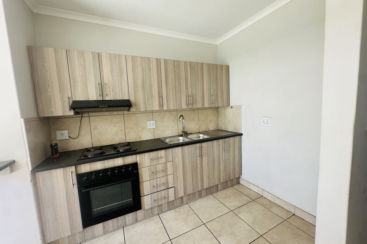 A functional kitchen featuring wood-look cabinetry, built-in oven and hob, double sink, and tiled flooring, offering a clean and practical workspace.