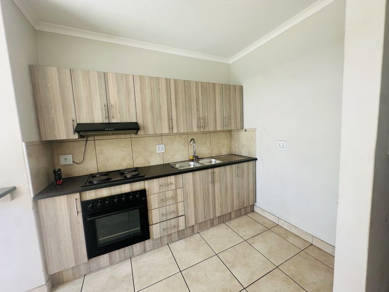 A functional kitchen featuring wood-look cabinetry, built-in oven and hob, double sink, and tiled flooring, offering a clean and practical workspace.